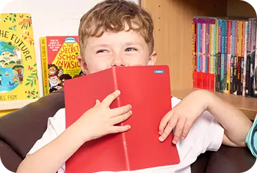 menino de escola segurando o livro vermelho na frente do rosto